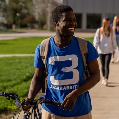 Student walking with his bike across campus