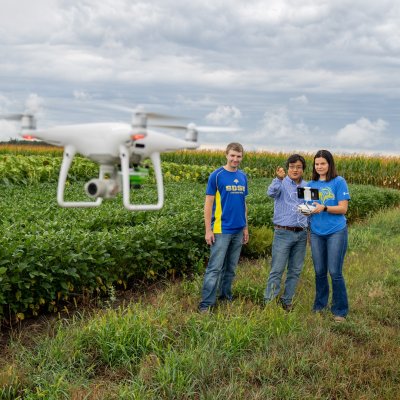 Two students and a faculty member standing by a field flying a drone.